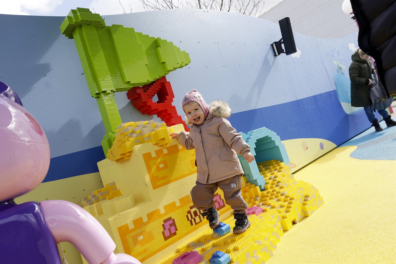 Lite barn leker på en LEGO-bygget strand med klosse-palme og sandslott i et småbarnsområde på Legoland Billund.
