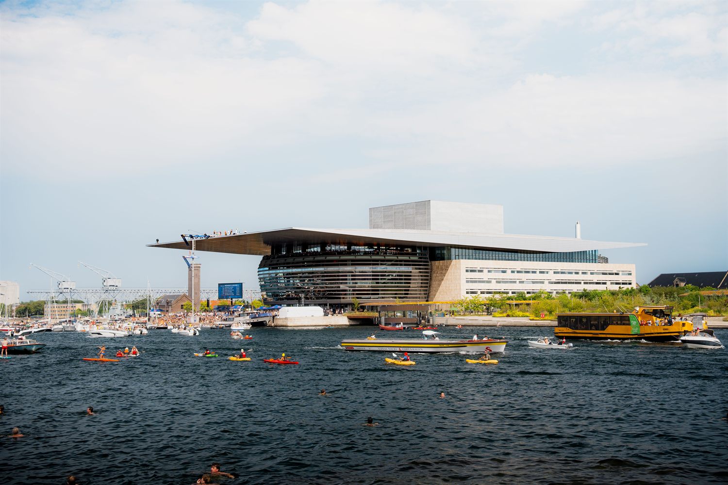 Operaen i København sett fra havnen en sommerdag, med båter og kajakker på vannet.