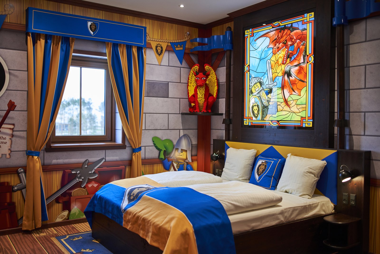 Drageridder-rom på Castle Hotel med blått og gult sengetøy, glassmaleri med drage og ridderutstyr på veggen.