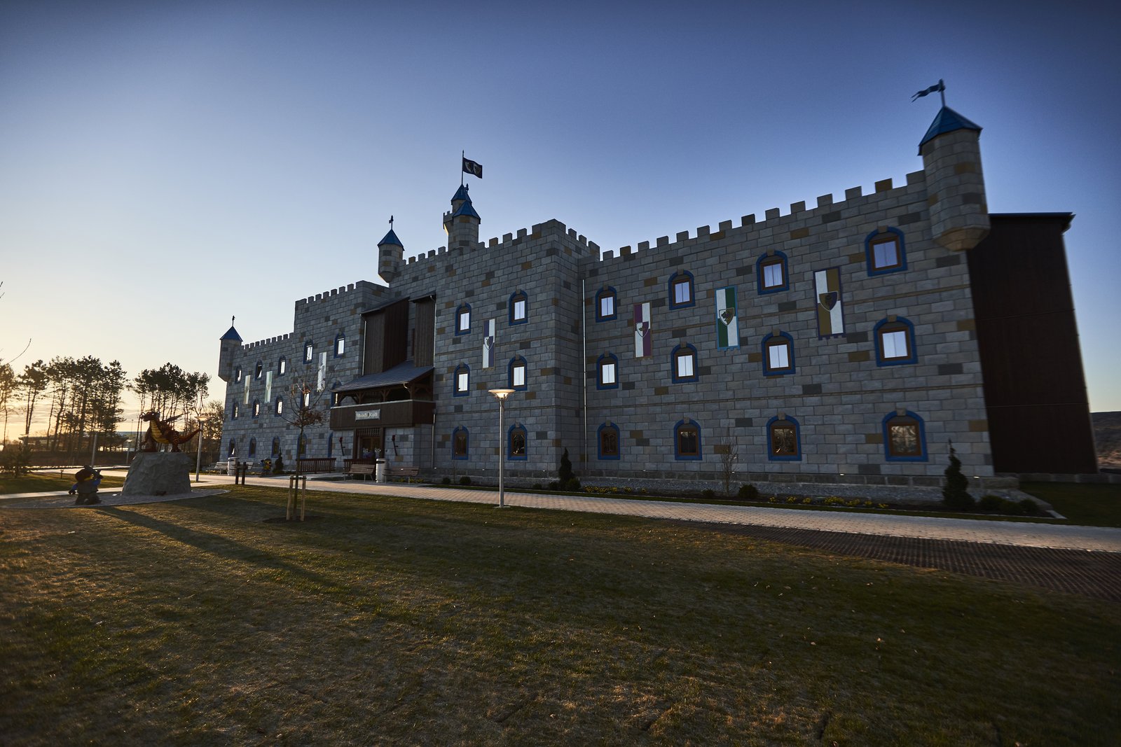 LEGOLAND Castle Hotel i skumringen – en lys borg med tinder, tårn og flagg, med plen og gangvei foran.